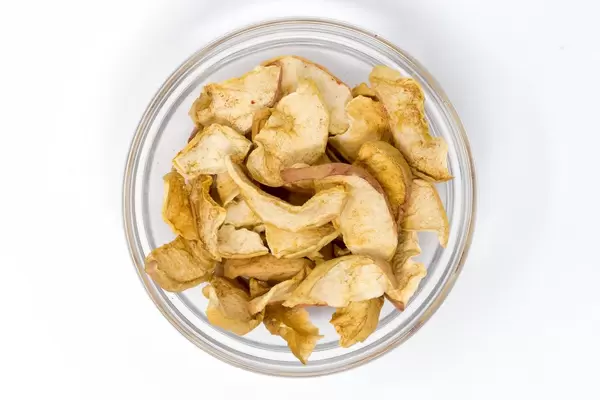 Aufsicht Dörrwerk - Getrocknete Apfel Chips mit Zimt in Glaschale auf weißem Hintergrund