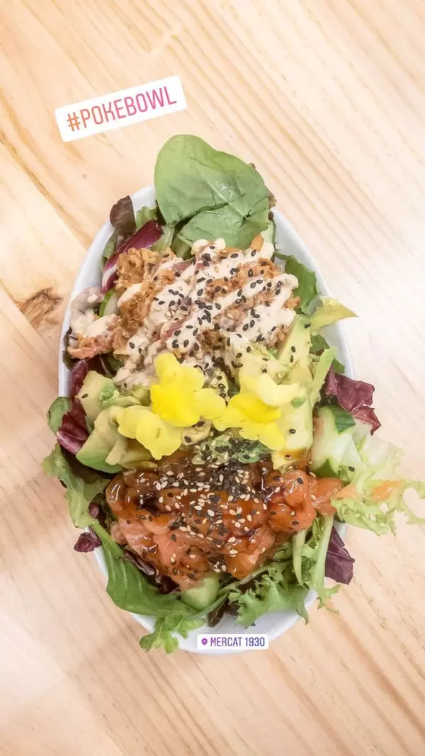 Aufsicht - Ein Salat aus Baby-Spinat, Rucola, Avocado, Tomaten, Dressing, Blüten und Sesam in einem ovalen Teller