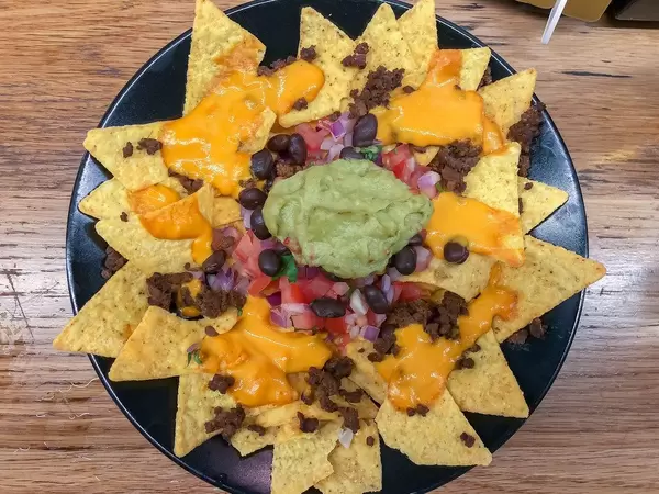 Aufsicht - Eine Portion Nachos mit Käsesauce, Rinderhackfleisch, roten Bohnen, Tomaten, Zwiebeln und Guacamole Avocado-Dip auf einem schwarzen Teller