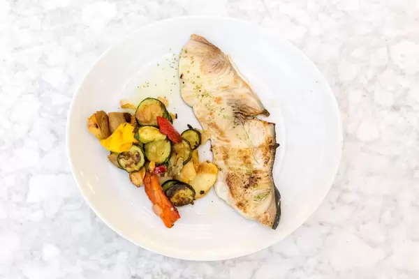 Aufsicht - Gegrillter Schwertfisch mit Gemüse auf einem weißen Teller auf Marmor-Untergrund