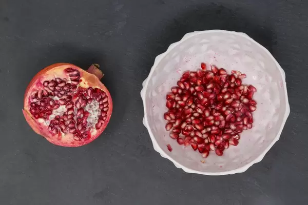 Aufsicht halber Granatapfel mit Granatapfelkernen in weißer Schale auf schwarzer Schieferplatte