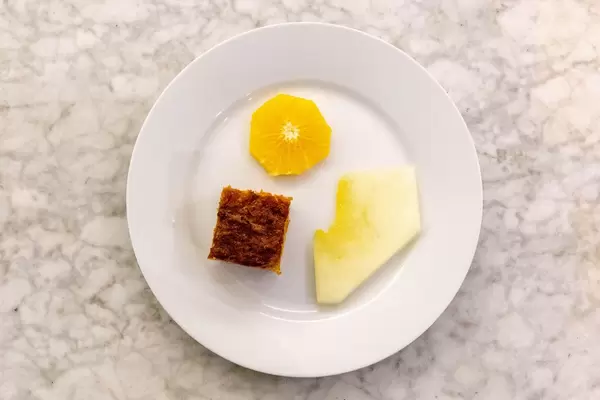 Aufsicht - Karottenkuchen auf weißem Teller mit einer Scheibe Orange und Honigmelone