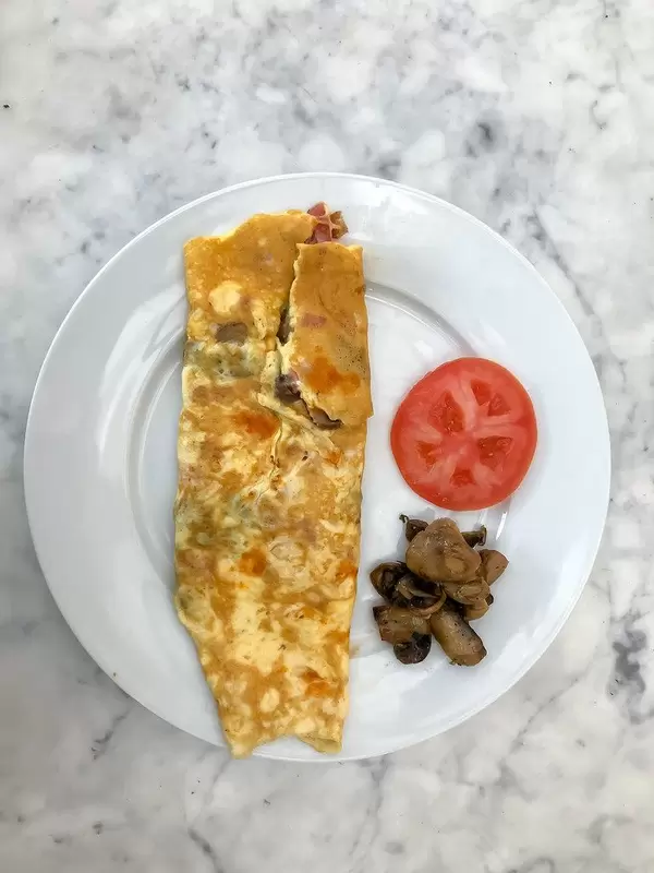 Aufsicht - Schinken-Pilz Omelette mit Pilzen und einer Scheibe Tomaten auf einem weißen Teller