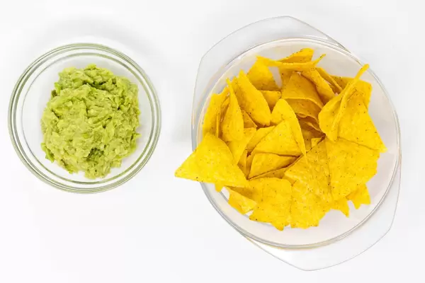 Aufsicht von Nachos und Guacamole in Schälchen auf weißem Hintergrund