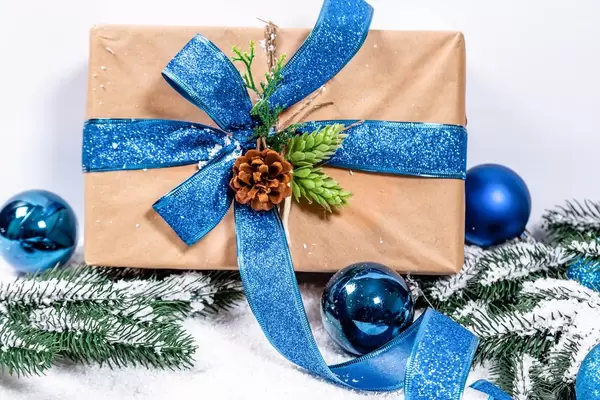 Aufsicht von schneebedecktem Weihnachtsgeschenk in Naturpapier und blauer Schleife, geschmückt mit Tannenzapfen