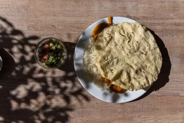 Aufsicht von Tikki Masala Hähnchen mit Reis und Fladenbrot auf weißem Teller mit gemischtem Salat als Beilage