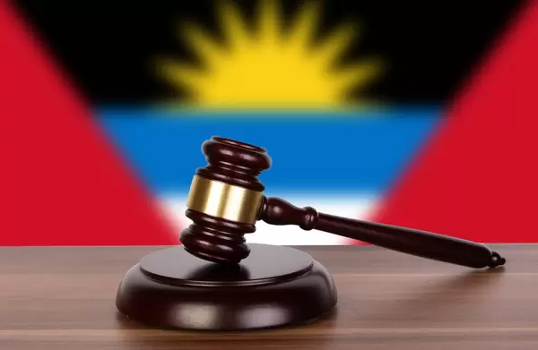 Auktionshammer / Richterhammer auf einem Holzuntergrund, vor der Flagge von Antigua und Barbuda