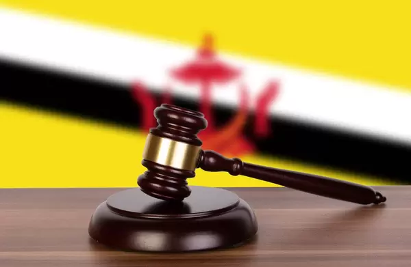 Auktionshammer / Richterhammer auf einem Holzuntergrund, vor der Flagge von Brunei