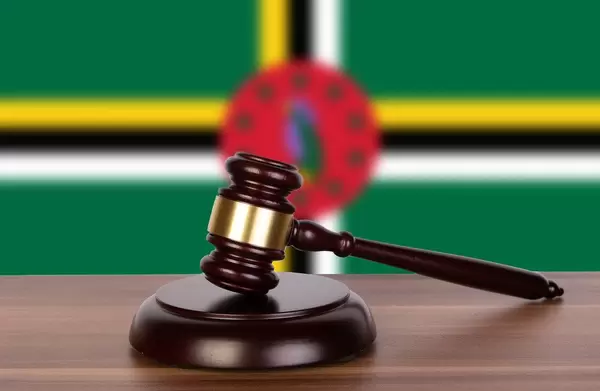 Auktionshammer / Richterhammer auf einem Holzuntergrund, vor der Flagge von Dominica