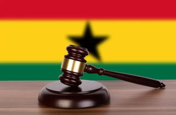 Auktionshammer / Richterhammer auf einem Holzuntergrund, vor der Flagge von Ghana