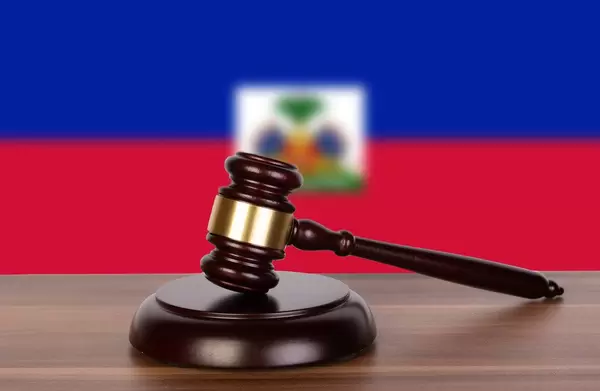 Auktionshammer / Richterhammer auf einem Holzuntergrund, vor der Flagge von Haiti