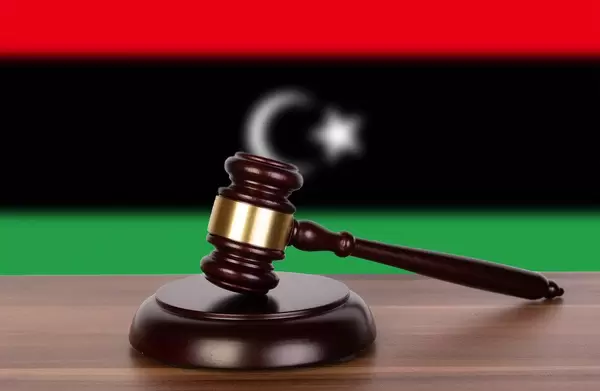 Auktionshammer / Richterhammer auf einem Holzuntergrund, vor der Flagge von Libyen