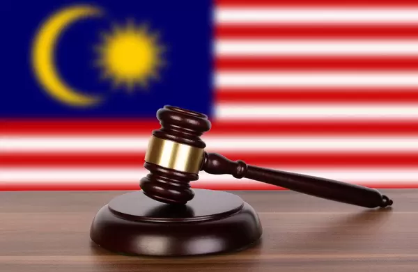 Auktionshammer / Richterhammer auf einem Holzuntergrund, vor der Flagge von Malaysia