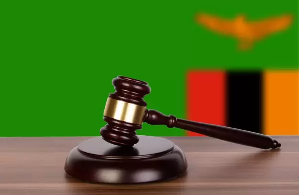 Auktionshammer / Richterhammer auf einem Holzuntergrund, vor der Flagge von Sambia