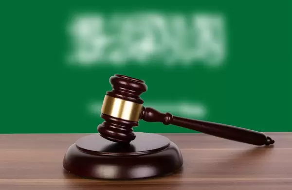 Auktionshammer / Richterhammer auf einem Holzuntergrund, vor der Flagge von Saudi-Arabien