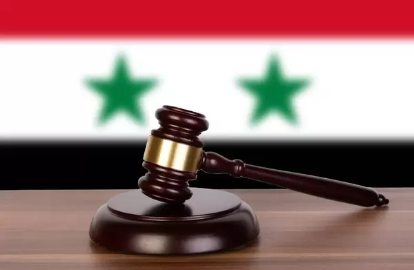 Auktionshammer / Richterhammer auf einem Holzuntergrund, vor der Flagge von Syrien