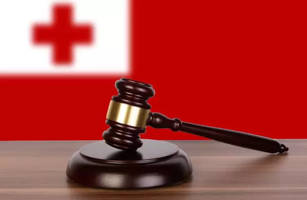 Auktionshammer / Richterhammer auf einem Holzuntergrund, vor der Flagge von Tonga
