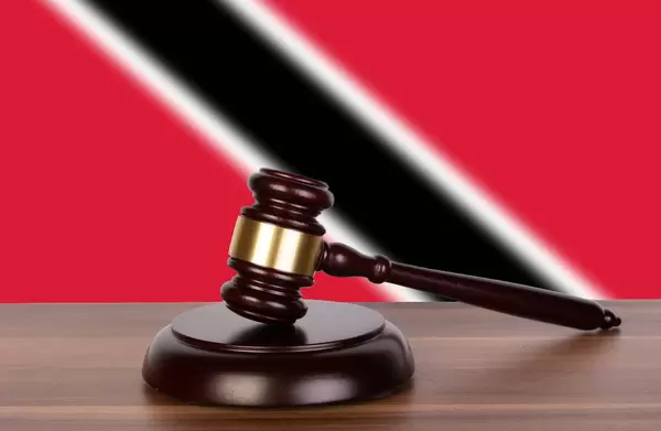 Auktionshammer / Richterhammer auf einem Holzuntergrund, vor der Flagge von  Trinidad and Tobago
