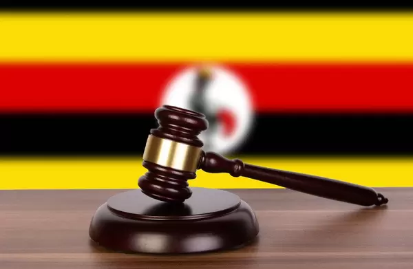 Auktionshammer / Richterhammer auf einem Holzuntergrund, vor der Flagge von Uganda