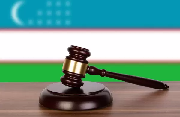 Auktionshammer / Richterhammer auf einem Holzuntergrund, vor der Flagge von Usbekistan