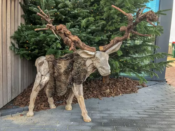 Aus Holz geschnitzter Elch mit Hörnern aus Ästen vor Tannenbaum
