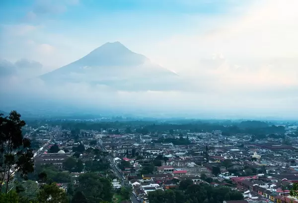 Ausblick über Antigua in Guatemala, im Hintergrund imposanter, von Wolken teilweise verhüllter Vulkan