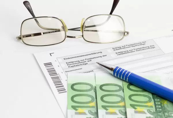 Ausfüllen der Steuererklärung mit einem Kugelschreiber, einer Brille und Euroscheinen