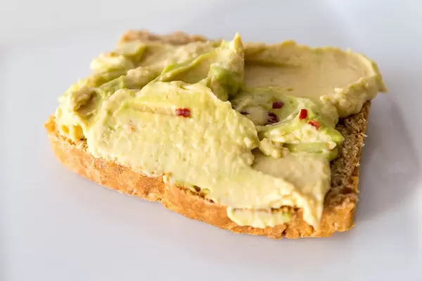 Ausgewogener Brotaufstrich mit Avocado-Hummus und Gewürzen, isoliert vor weißem Hintergrund