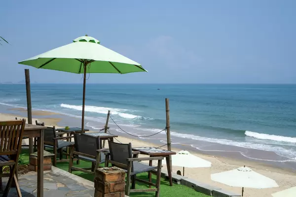 Außenbereich mit Stühlen, Tischen und Sonnenschirm im Sound of Silence Cafe mit Blick auf das Meer am An Bang Strand in Hoi An, Vietnam