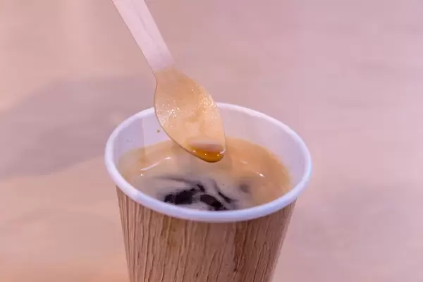 Automatenkaffee in umweltfreundlichem Einwegbecher mit Holzlöffel vor beigem Hintergrund