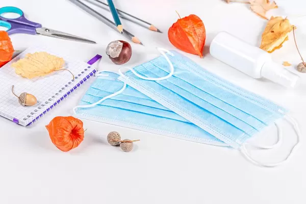 Autumn dry leaves, chestnut and acorns with medical masks and school supplies