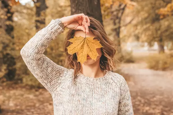 Autumn portrait girl covers her face with maple leaf