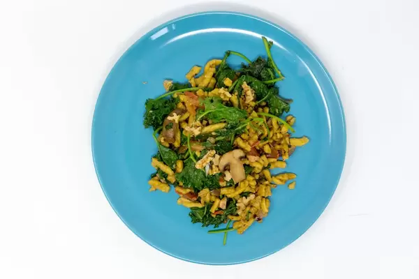 Autumn Spätzle Noodles with kale, mushrooms, tomatoes and roasted walnuts on a blue plate