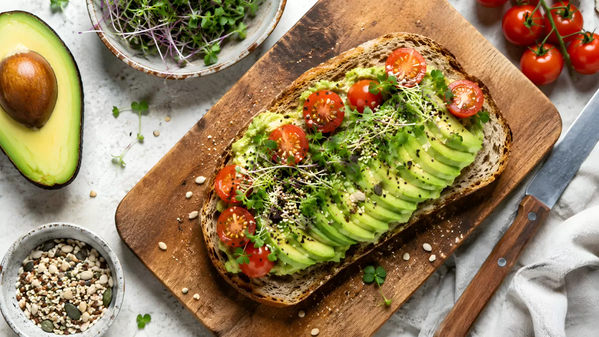 Avocado-Toast mit Tomaten und Microgreens auf Holzbrett