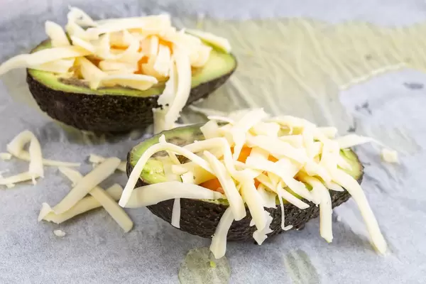 Avocadohälften mit rohen Eiern und geriebenem Käse auf einem Backpapier