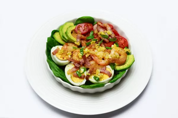 Avocadosalat mit ganzen Garnelen, gebratenem Speck, halbierten Cherrytomaten, Spinat und gekochten Eiern