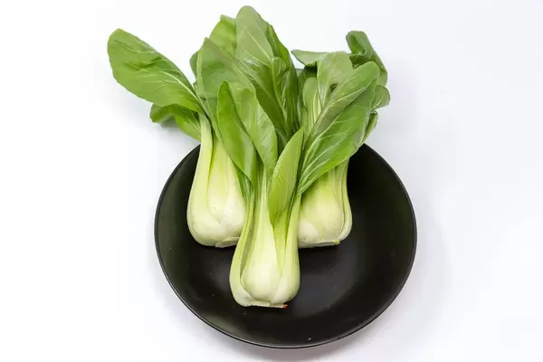 Baby Pak Choi auf schwarzem Teller auf weißem Hintergrund
