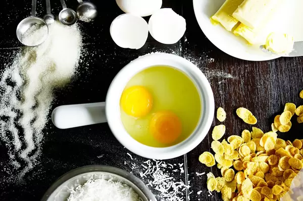 Back-Zutaten für ein Rezept auf einem Tisch - Eier, Kornflakes, Zucker und Butter  - Aufsicht