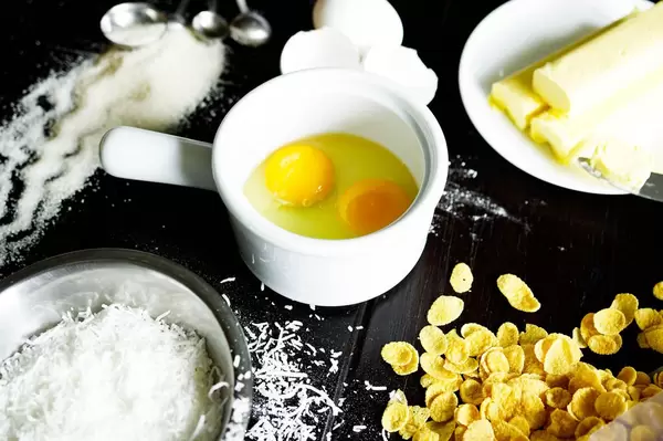Back-Zutaten für ein Rezept auf einem Tisch - Eier, Kornflakes, Zucker und Butter