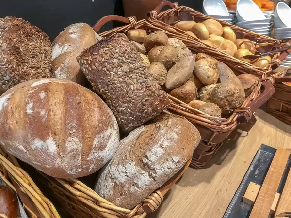 Bäckereiauslage am Frühstücksbüfett, mit verschiedenen Broten, Vollkorn-Brötchen mit Kernen und normalen Brötchen, in einfachen Holzkörben