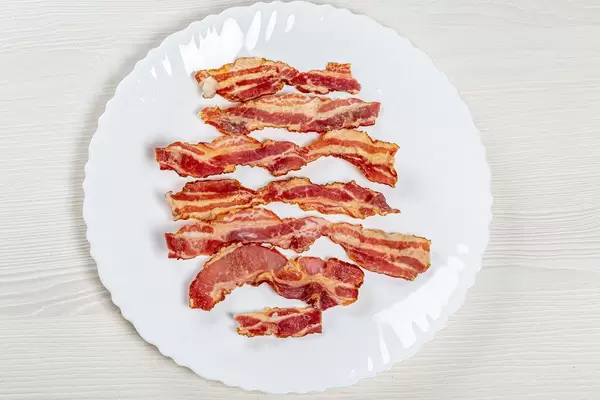 Bacon fried slices in plate, top view on white wooden table