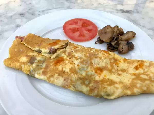 Bacon-mushrooms Omelette witch grilled mushrooms and a slice of tomato on the side