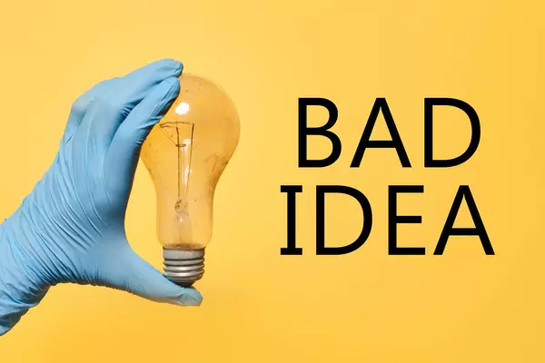 Bad idea - hand in medical gloves holding an old dirty bulb over yellow background