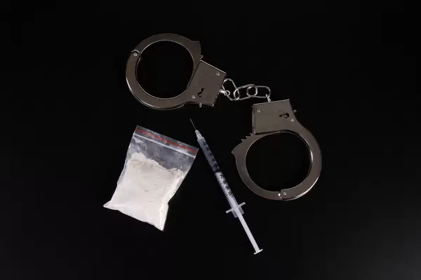 Bag of cocaine with syringe and handcuffs on black table