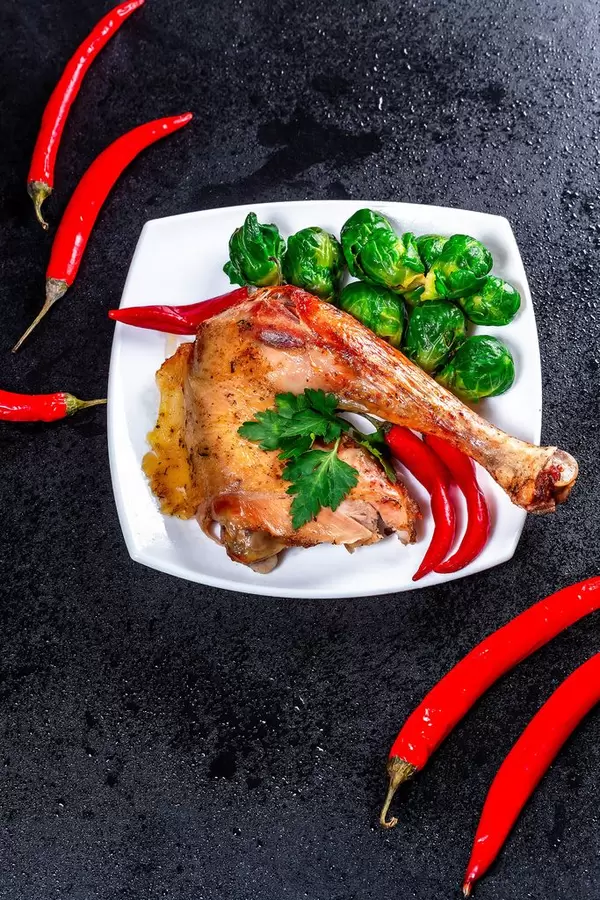 Baked chicken leg with Brussels sprouts and chili pepper on black background (Flip 2019)
