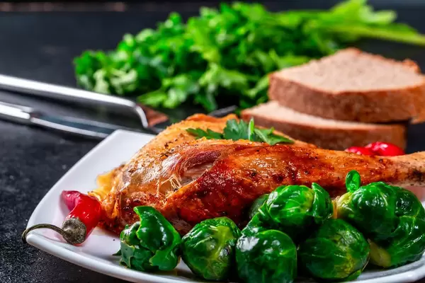 Baked chicken leg with Brussels sprouts on a plate with black bread and parsley
