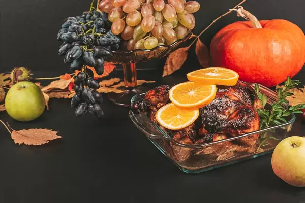 Baked chicken on a dark background with pumpkin, fruits and autumn leaves