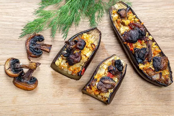 Baked eggplant with vegetables, couscous and mushrooms on a wooden background. Top view