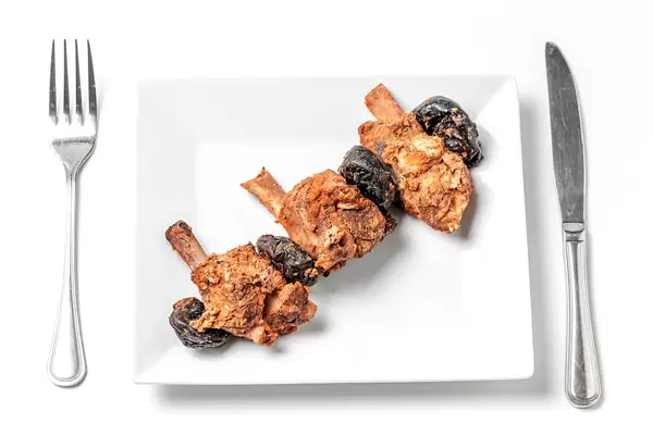Baked pork ribs with prunes on a white plate with a knife and fork