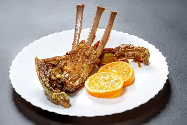 Baked ribs of young lamb with slices of fresh orange in a plate on a black background (Flip 2019)